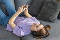 Relax at home, positive thinking. Happy young woman lying at home on the couch with headphones and mobile phone Royalty Free Stock Photo