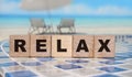Relax - an inscription on wooden cube blocks on sunny beach beckground with reflection
