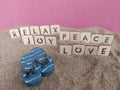 Relax peace joy love inspirational words written on sand with blue flip flops and pink background