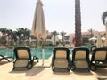 Relax pool with clear blue water with sunbeds for sunbathing with sun umbrellas against the backdrop of green palms and white buil Royalty Free Stock Photo