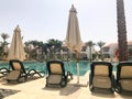 Relax pool with clear blue water with sunbeds for sunbathing with sun umbrellas against the backdrop of green palms and white buil Royalty Free Stock Photo