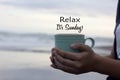 Relax. It`s Sunday. Hello Sunday weekend concept with a person holding a cup of coffee in hand on beach background. Happy Sunday. Royalty Free Stock Photo