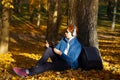 Asian young man  lean the tree and looking Tablet as a listening to music in autumn season with a sunny light in the Royalty Free Stock Photo