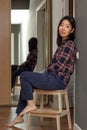 Relaxed adult asian woman sitting on chair in hallway at home, female reflection in mirror of apartment closet