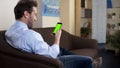 Relaxed adult male on couch holding green screen smartphone, modern technology