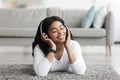 Relaxed african american lady listening music in wireless headphones while lying with closed eyes on floor carpet Royalty Free Stock Photo