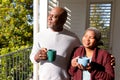 Relaxed african american senior couple drinking coffee standing on balcony in sun Royalty Free Stock Photo