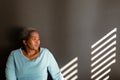 Relaxed african american senior woman sitting at wall in ray of light