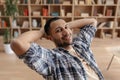 Relaxed arab man resting at home, holding hands behind head and smiling at camera, enjoying silence and comfort