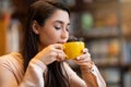 Relaxed arab woman smelling aromatic coffee with closed eyes and feeling harmony, sitting at cafe, copy space