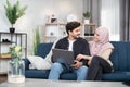 Relaxed Arabian Muslim couple in casual wear, using a laptop pc together for watching online content or shopping