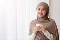 Relaxed arabic woman in hijab with cup of coffee near window Royalty Free Stock Photo