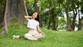 Relaxed Asian female sitting under the tree, stretching and massaging her neck Royalty Free Stock Photo