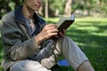 Relaxed Asian male college student chilling in the greenery park on the weekend, reading a book Royalty Free Stock Photo