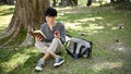 Relaxed Asian male college student eating apple while reading a book under the tree in the park Royalty Free Stock Photo