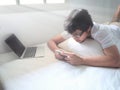 Relaxed Asian man with mobile smart phone lying down on the bed in morning Royalty Free Stock Photo