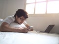 Relaxed Asian man with mobile smart phone lying down on the bed in morning Royalty Free Stock Photo