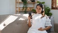 Relaxed Asian pregnant woman wearing headphones, listening to music in her living room Royalty Free Stock Photo