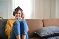 Relaxed Asian woman sits on the sofa, using mobile phone and listening music on headphones Royalty Free Stock Photo