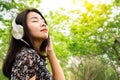 Relaxed Asian woman wearing headphone enjoying the music out doors while walking in a green park