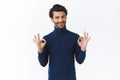 Relaxed and assured, assertive handsome bearded guy in blue high neck sweater, say everything alright, showing okay