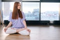 Relaxed attractive young woman meditating sitting on floor in lotus pose on background of window in light office room. Royalty Free Stock Photo