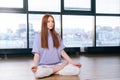 Relaxed attractive young woman meditating sitting on floor in lotus pose on background of window in light office room. Royalty Free Stock Photo