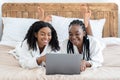 Relaxed black girlfriends reading beauty blog, laying on bed