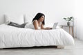 Relaxed black woman lying in bed and using laptop computer, working remotely, chatting or browsing social media Royalty Free Stock Photo