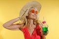 Relaxed blonde woman in sunglasses, red swimsuit and straw hat smiling with eyes closed, adjusting her hat and holding Royalty Free Stock Photo