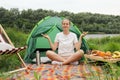 Relaxed calm woman with bun hairstyle sitting with crossed legs in lotus pose meditating practicing yoga in open air, being