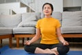 Relaxed calm young Asian woman practicing yoga, practicing a lotus pose and meditating