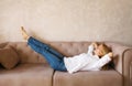 Relaxed caucasian young woman resting with closed eyes and folded hands behind the head while lying on couch in the living room at Royalty Free Stock Photo