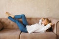 Relaxed caucasian young woman resting with closed eyes and folded hands behind the head while lying on couch in the living room at Royalty Free Stock Photo