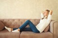 Relaxed caucasian young woman resting with closed eyes and folded hands behind the head while lying on couch in the living room at Royalty Free Stock Photo