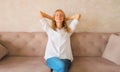 Relaxed caucasian young woman resting with closed eyes and folded hands behind the head while sitting on couch in the living room Royalty Free Stock Photo