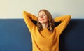 Relaxed caucasian young woman resting with closed eyes and folded hands behind the head sitting on the couch in room at home Royalty Free Stock Photo