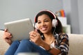 Relaxed charming african american woman in headphones listening to music and choosing with finger on tablet screen Royalty Free Stock Photo