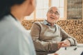 Confident pleasant old man sitting with windows behind