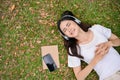 Relaxed and chilling young Asian woman listening to music , smiling, eyes closed and lying on grass Royalty Free Stock Photo