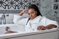 Good-looking relaxed confident dark-skinned mixed race woman in bathrobe sitting in bathtub having rest