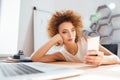 Relaxed cute curly young woman using mobile phone in office Royalty Free Stock Photo