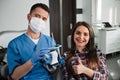 Relaxed at the dentist. Happy female patient sitting in a dental chair smiling to the camera with her dentist holding false tooth