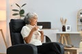 Relaxed elderly woman sitting on armchair drinking hot tea and looking away Royalty Free Stock Photo