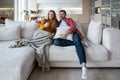 Relaxed family couple watch TV together sitting on cozy sofa at home enjoying favourite movie series