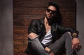 Relaxed fashion man in sunglasses and leather jacket is sitting Royalty Free Stock Photo