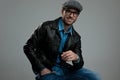 Relaxed fashion man wearing leather jacket and flat cap sitting Royalty Free Stock Photo