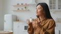 Relaxed girl Asian korean woman in domestic kitchen with cup of coffee drinking hot herbal tea multiethnic lady Royalty Free Stock Photo