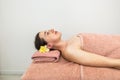 A relaxed girl with a flower in her hair is lying face up on the massage table, waiting for a massage. Beautiful girl in the spa Royalty Free Stock Photo