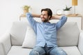 Relaxed Guy Sitting Holding Hands Behind Head On Sofa Indoor
